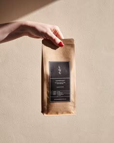 a woman's hand holding a bag of coffee on top of a beige wall