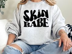 a woman sitting on a couch wearing a sweatshirt with the words skin babe printed on it