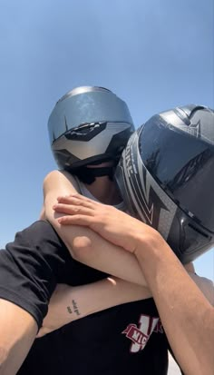 two people hugging each other with helmets on their heads and one person wearing a black shirt