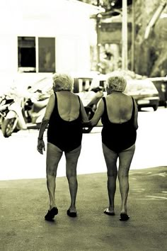 two women walking down the street with their backs to each other, both wearing black swimsuits