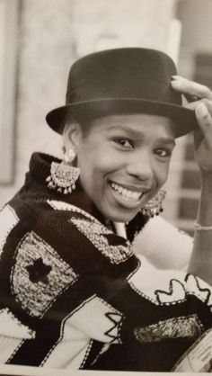 a black and white photo of a smiling woman in a hat with earrings on her head