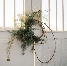 a wreath hanging from the side of a white wall with greenery on it's sides