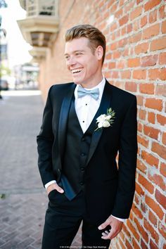 a man in a tuxedo standing next to a brick wall