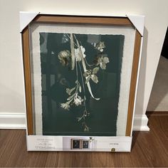 an image of flowers in a glass frame on the floor with wood floors and white walls