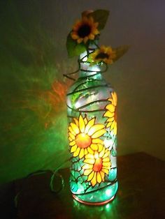 a glass vase with sunflowers on it sitting on a table next to a green light