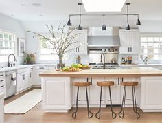 a large kitchen with white cabinets and wooden counter tops, along with stools that match the hardwood flooring