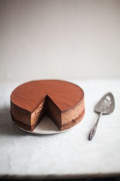 a chocolate cheesecake on a white plate next to a spoon