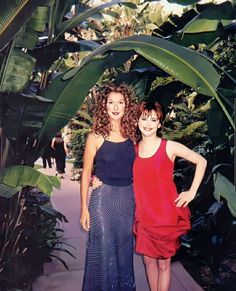 two women standing next to each other in front of plants