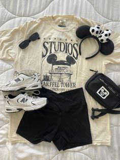 a white shirt with mickey ears and other items sitting on top of a bed next to a pair of shoes