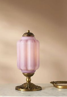 a pink glass lamp sitting on top of a white table next to a gold tray