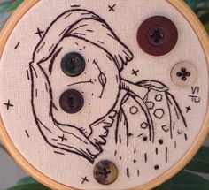 a close up of a embroidery on a piece of cloth with two buttons and a drawing of a woman