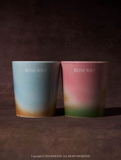 two cups sitting next to each other on top of a brown surface with the word rosino painted on them