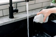 a person is holding a bottle and filling it with water from a faucet