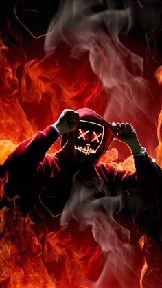 a person wearing a red mask and holding their hands up to their face in front of fire