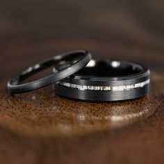 two black wedding bands sitting on top of a wooden table next to each other,