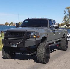 a large gray truck driving down a street next to a body of water on a sunny day