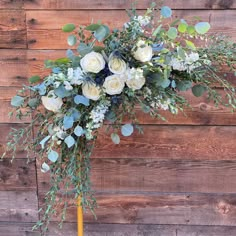 a bouquet of white roses and greenery on a yellow pole in front of a wooden wall