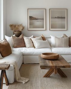 a living room with white couches and pillows on the walls, two pictures above them