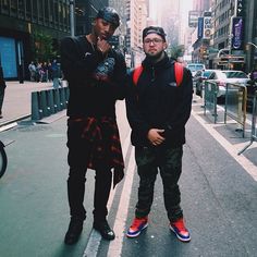 two young men standing next to each other on the street