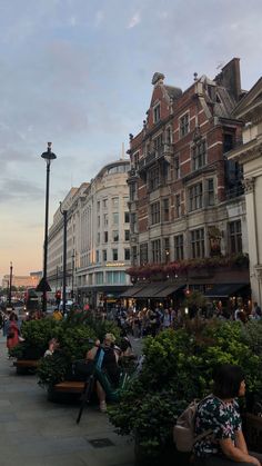 many people are sitting on benches in the middle of a city street with tall buildings