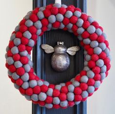 a red, grey and white wreath with a silver bee on it hanging from a black door