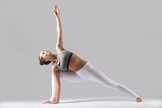 a woman in white tights and grey top doing a yoga pose with her hands up