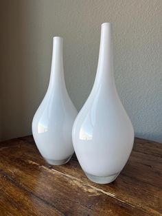 two white vases sitting on top of a wooden table