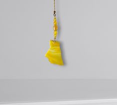 a yellow necklace hangs from a gold chain on a white wall in an empty room