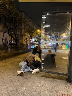 two people sitting on the ground in front of a glass bus stop door at night