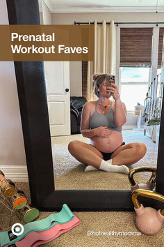 a pregnant woman sitting on the floor taking a selfie in front of a mirror