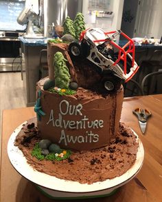 a birthday cake made to look like a monster truck on top of a hill with the words our adventure awaits written on it