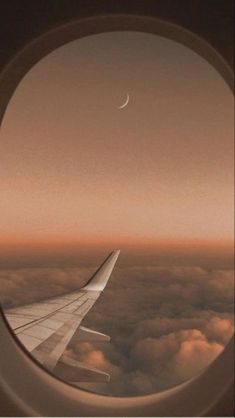 an airplane window looking out at the sky and clouds with a half moon in the distance