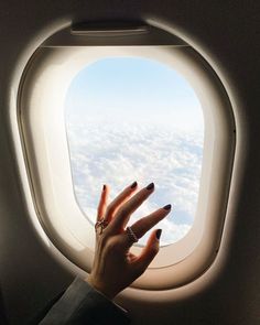 a woman's hand on the edge of an airplane window with clouds in the background