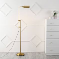 a floor lamp in the corner of a room with white walls and drawers on either side