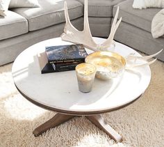 a table with two candles on it in front of a couch and deer antlers