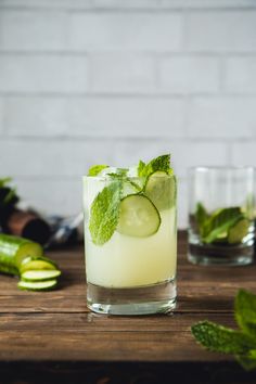 a glass filled with cucumber and mint on top of a wooden table next to other glasses