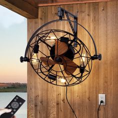 a person holding a remote control in front of a wall mounted fan with lights on it