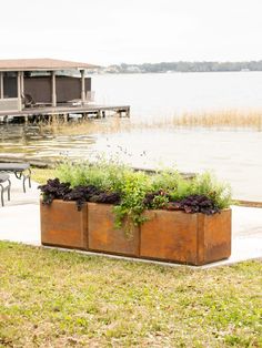 two wooden planters filled with plants next to a body of water in front of a dock