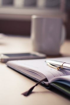 an open notebook with a pen on top of it next to a coffee cup and cell phone