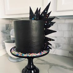 a black cake decorated with sprinkles and spikes on a table in a kitchen