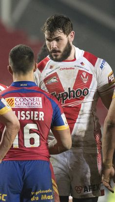 two men are talking to each other in a rugby game, one is wearing a red and blue uniform