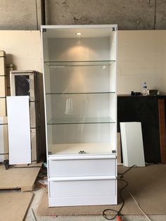 a tall white cabinet with glass shelves in the middle and other items on the floor