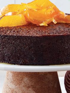 a chocolate cake with oranges on top is sitting on a white plate next to some candy