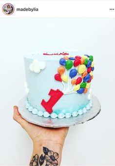 a hand holding a cake with balloons on it