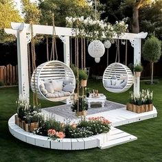 an outdoor area with swings, chairs and flowers on the grass in front of trees