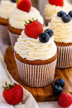 some cupcakes with white frosting and strawberries on top are sitting on a wooden board