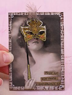 a hand holding a card with a masquerade mask on it's face