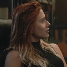 a woman with long hair sitting in a chair and looking off to the side while wearing a black top