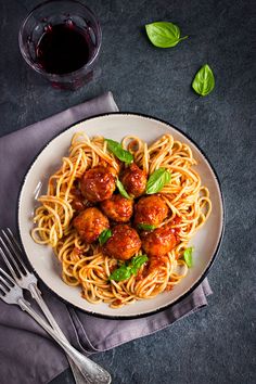 spaghetti with meatballs and basil on top, next to a glass of red wine