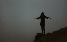 a woman standing on top of a hill with her arms outstretched